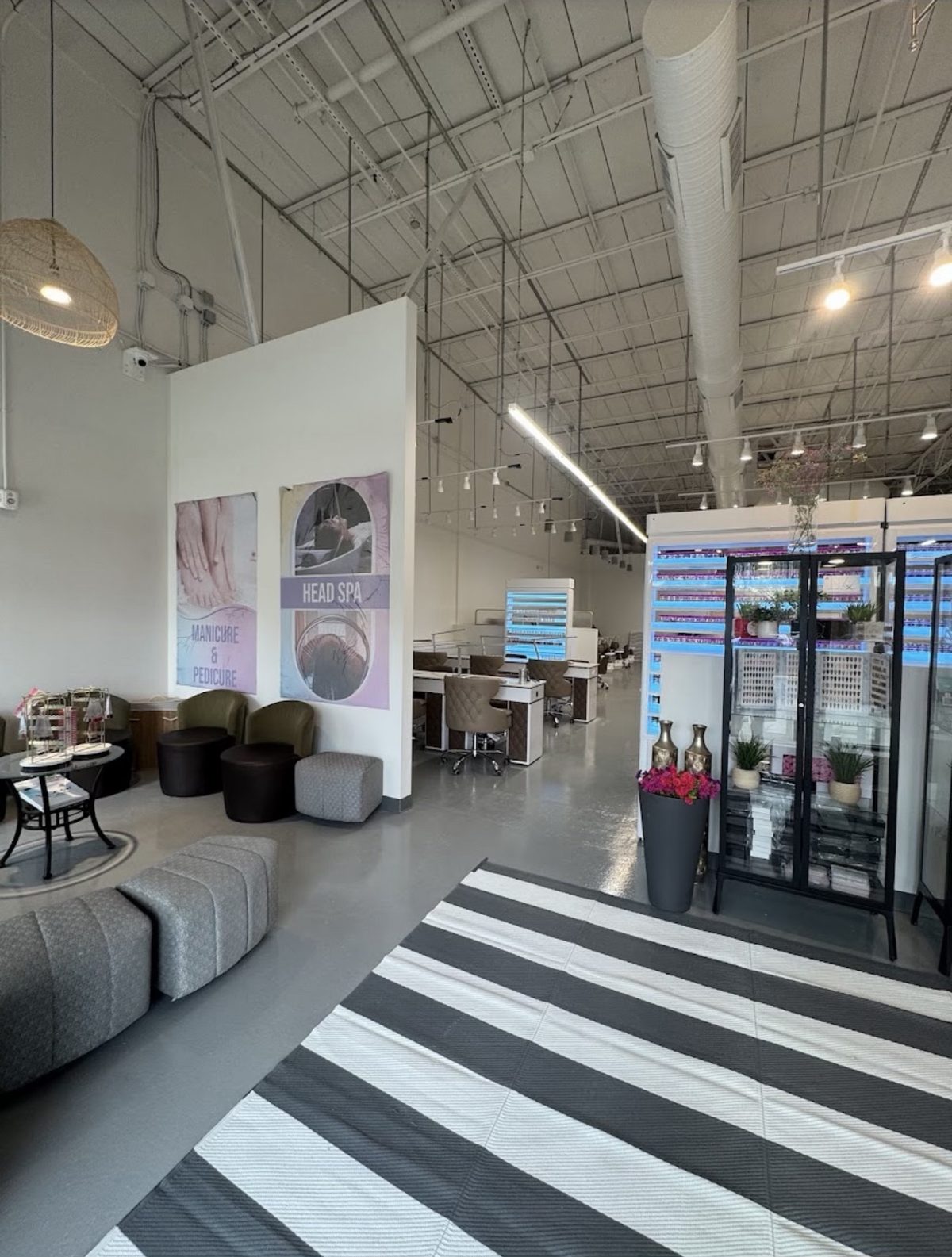 The waiting lounge, with soft chairs beside two large posters for manicure and pedicure and for head spa. A striped rug leads toward the manicure stations.