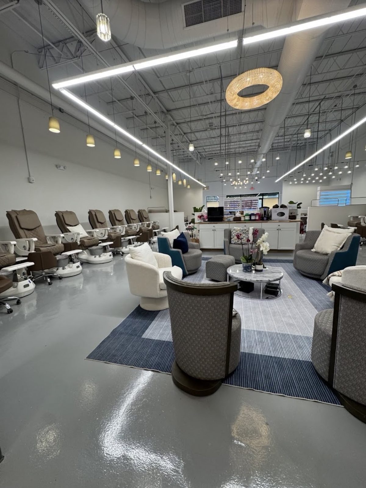 A long row of pedicure chairs beside the guest lounge, where soft chairs sit around a marble table with orchids under a round crystal light.